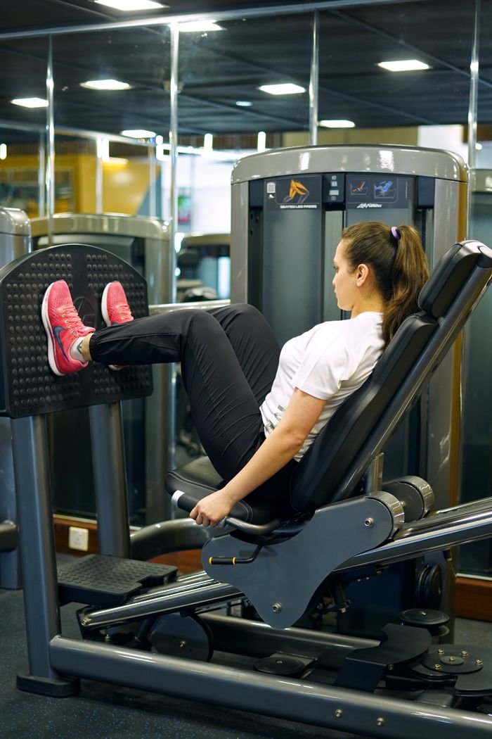 who-we-are Female athlete working out on a leg press machine in a modern gym.