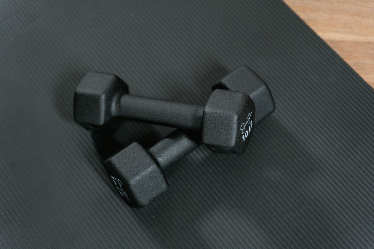 about-us Black dumbbells placed on a yoga mat, perfect for home workouts and strength training.